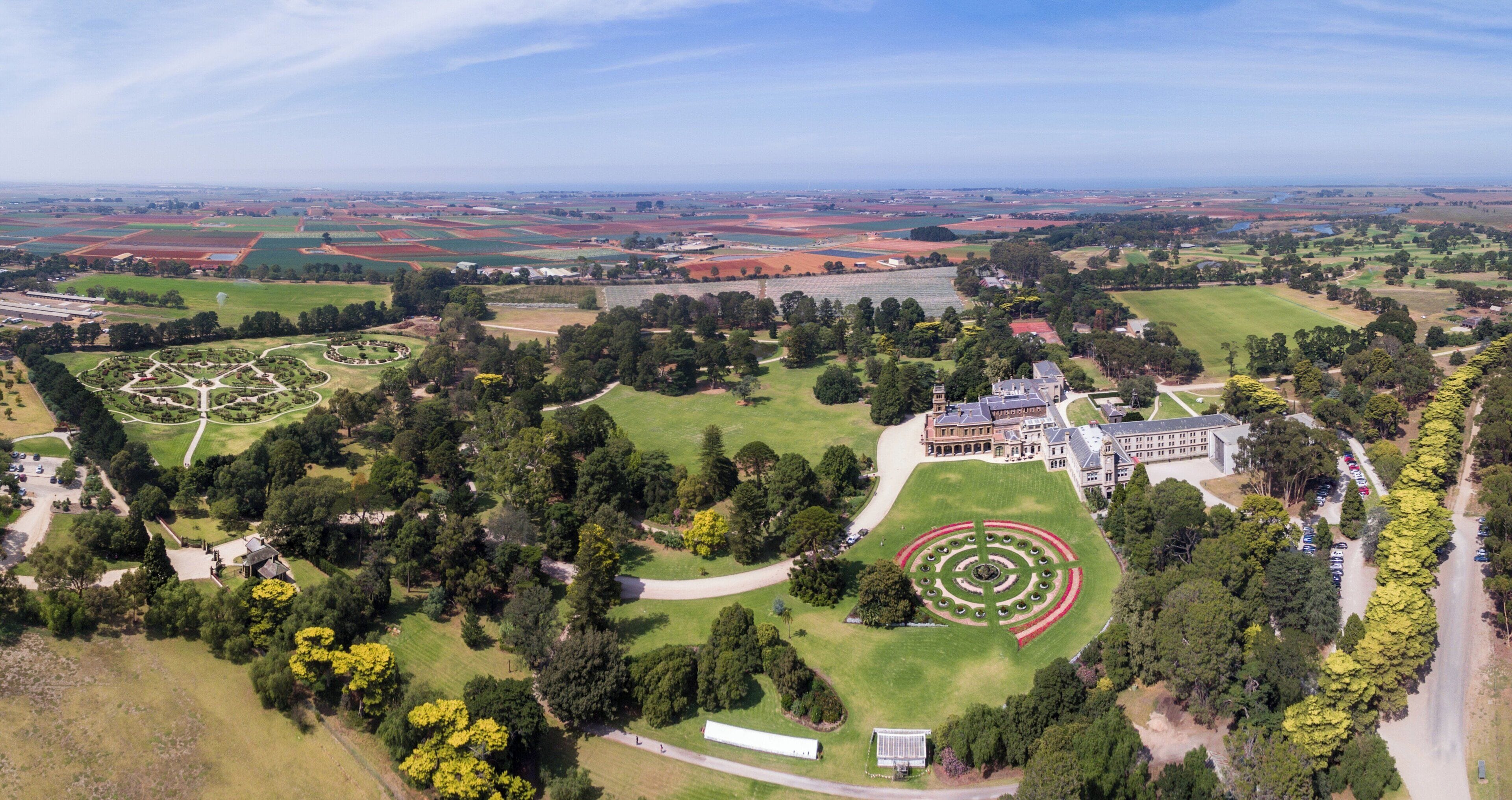 Vista aérea de una gran propiedad con jardines cuidados, un césped circular central y un edificio imponente.