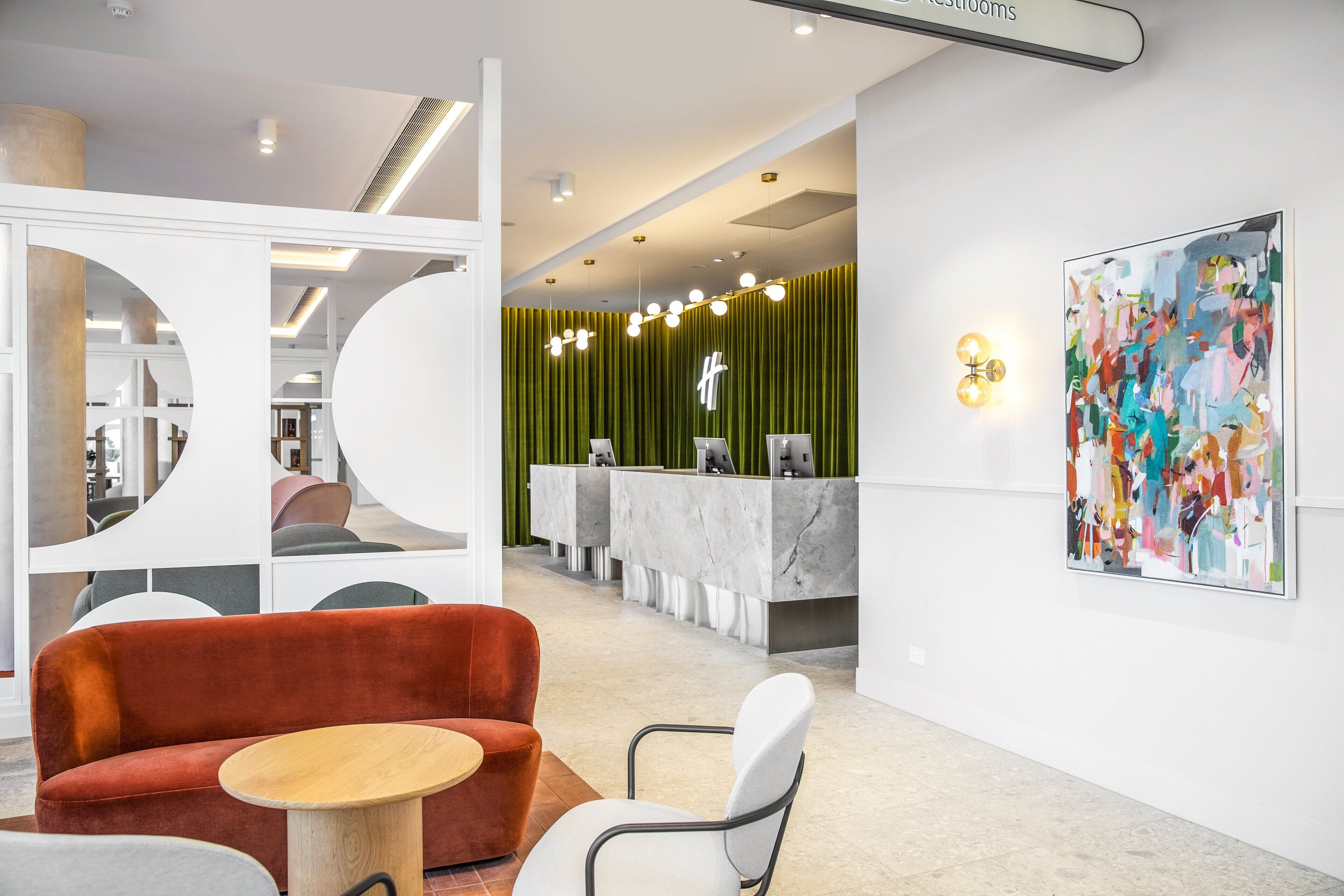A modern reception area with a reception desk, a seating area with a red sofa and a round table, and a large abstract painting on the wall.