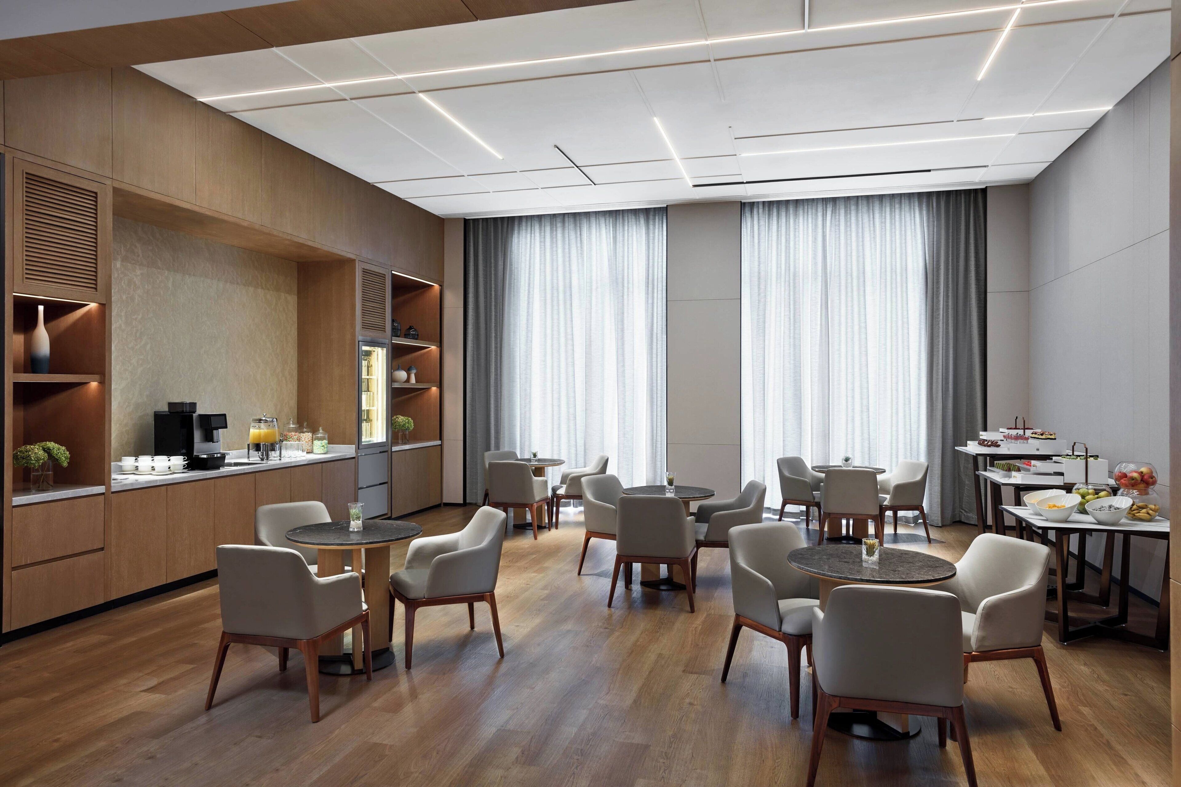 En moderne hotellobby med runde borde og stole, kaffestation og buffetområde.