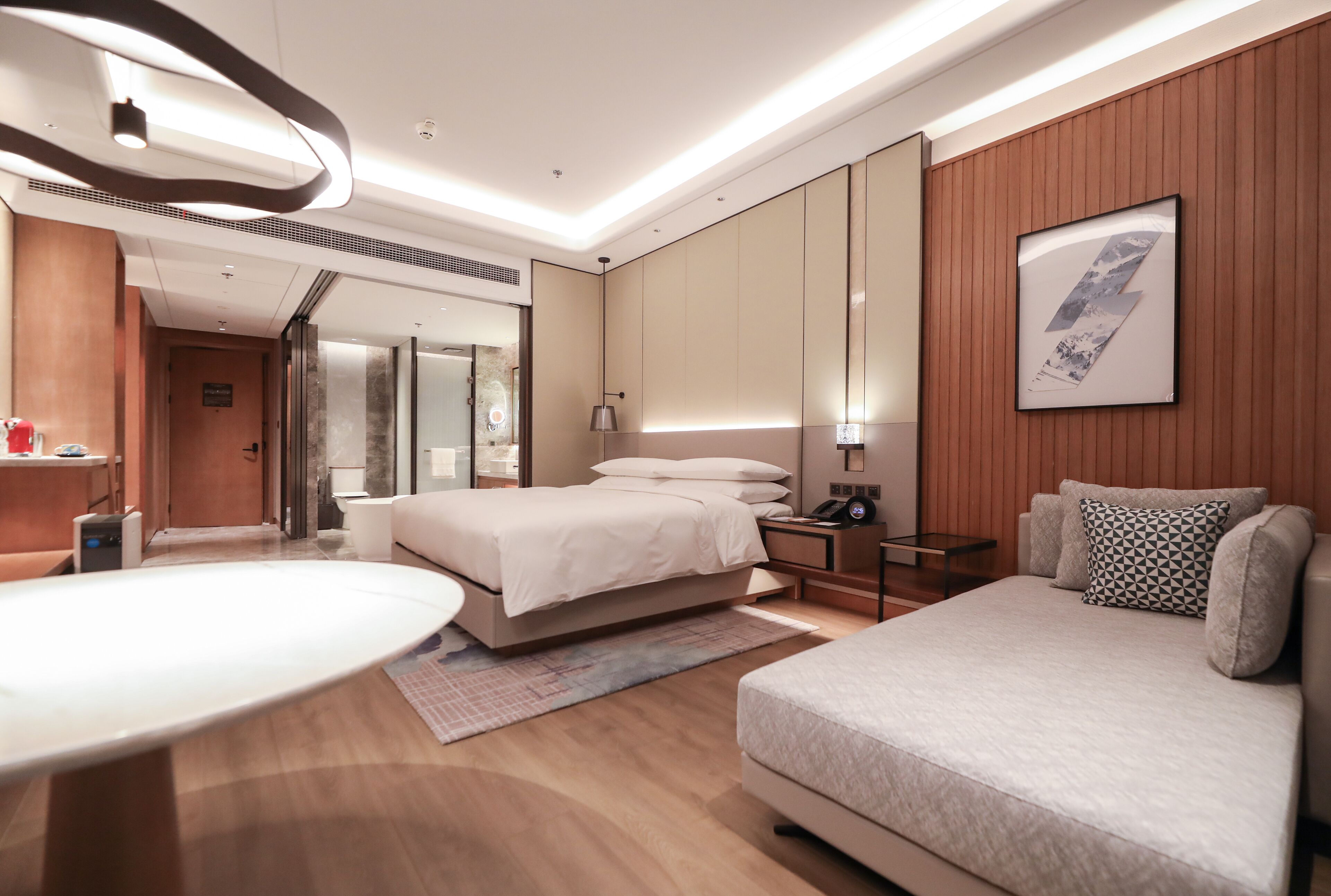 Una habitación de hotel moderna con una cama, un sofá, un escritorio y un espejo grande.