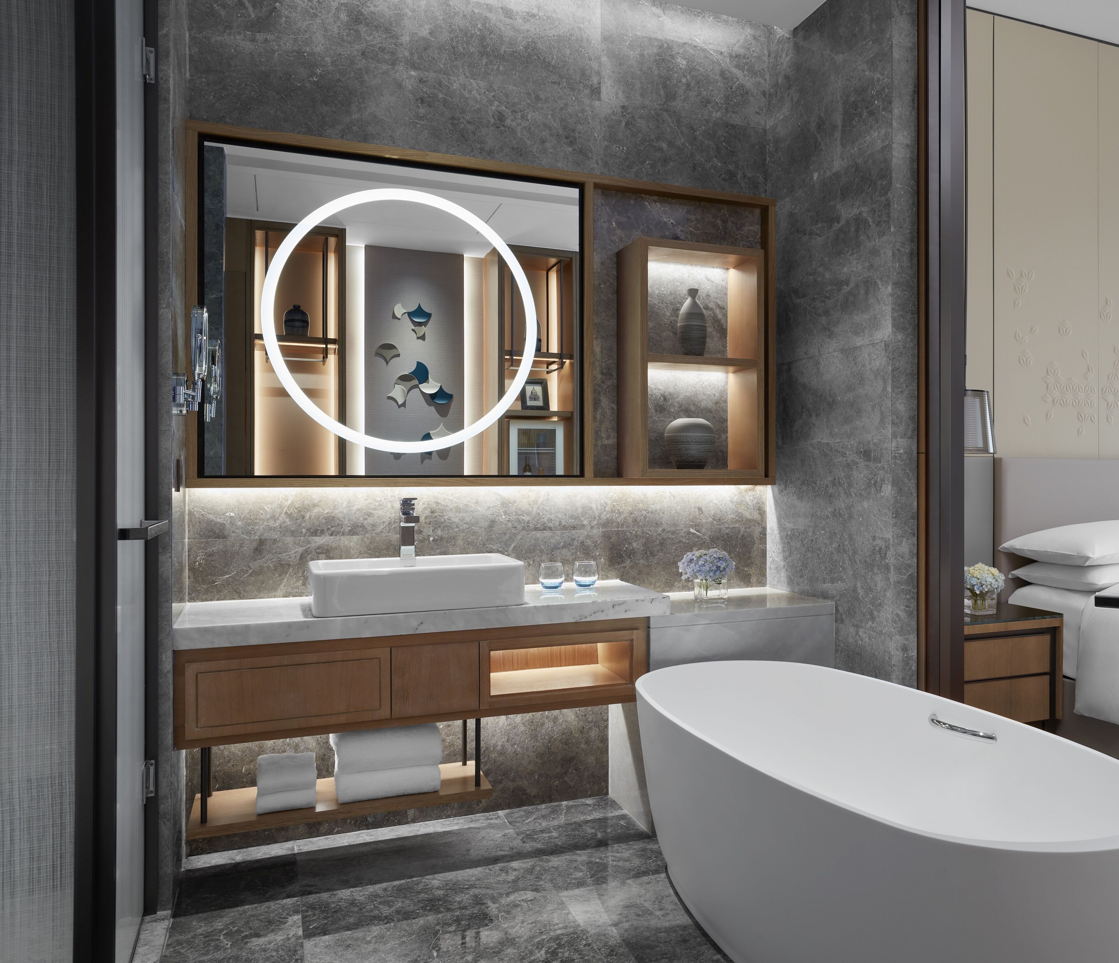 Un bagno moderno con una grande vasca, un mobile lavabo con specchio e uno scaffale a parete con oggetti decorativi.