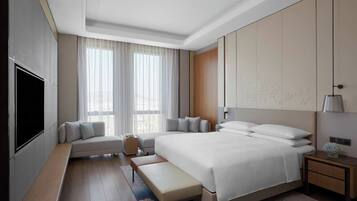 Habitación de hotel moderna con una cama grande, un banco, un televisor y una mesita de noche con lámpara.