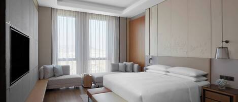 Habitación de hotel moderna con una cama grande, un banco, un televisor y una mesita de noche con lámpara.