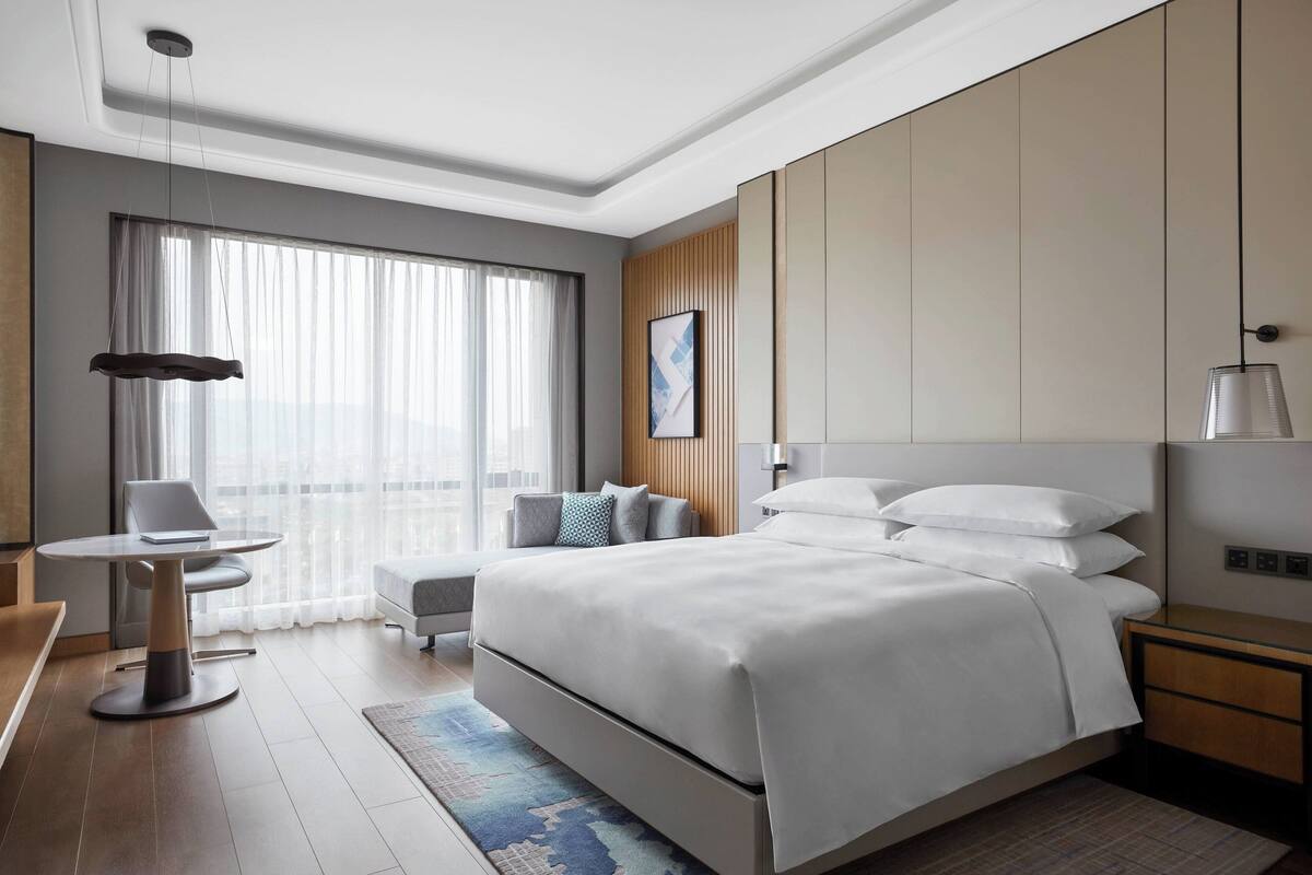 A modern hotel room with a large bed, a desk, and a chair.