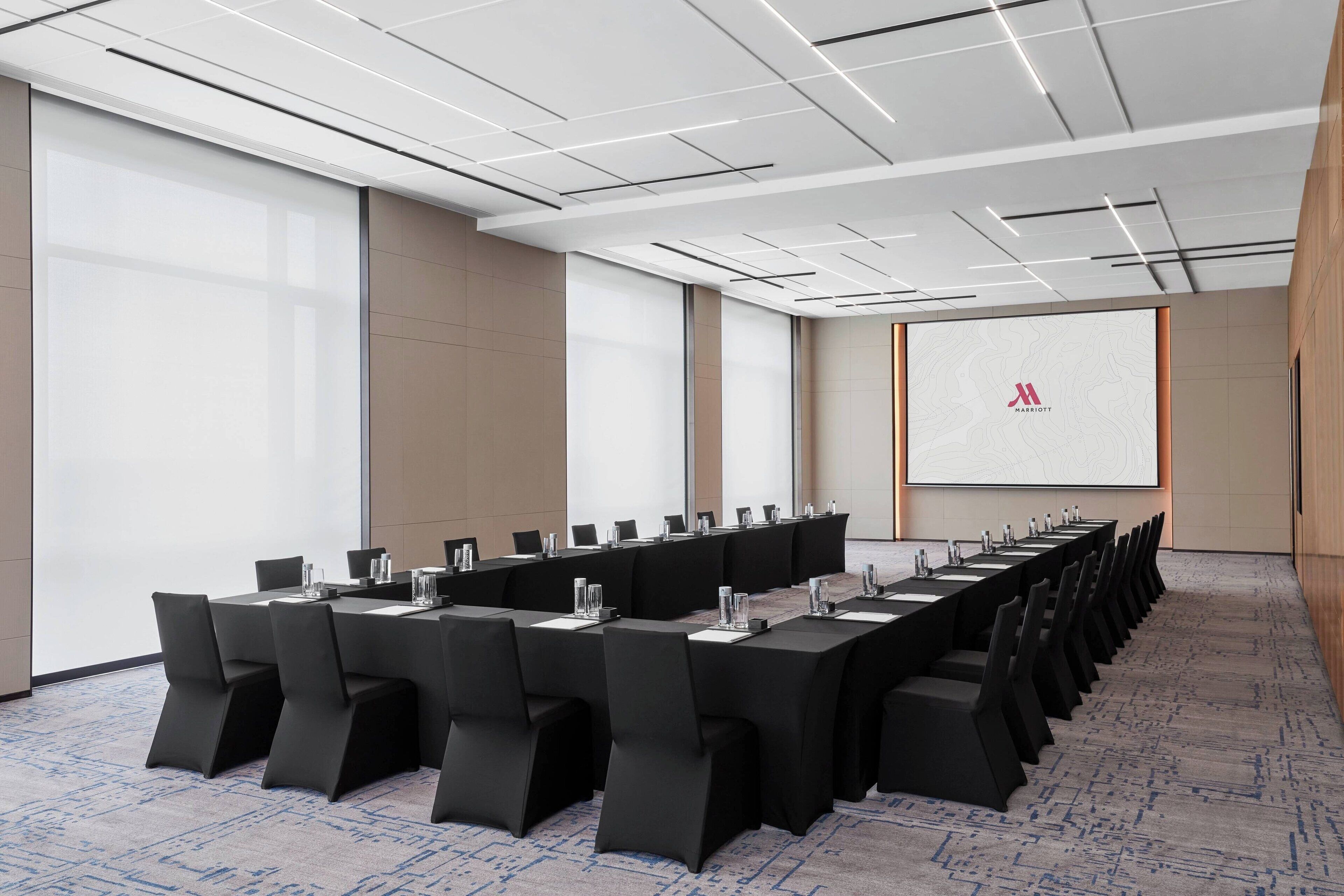 Un salón de conferencias con una larga mesa, sillas y una pantalla para presentaciones.
