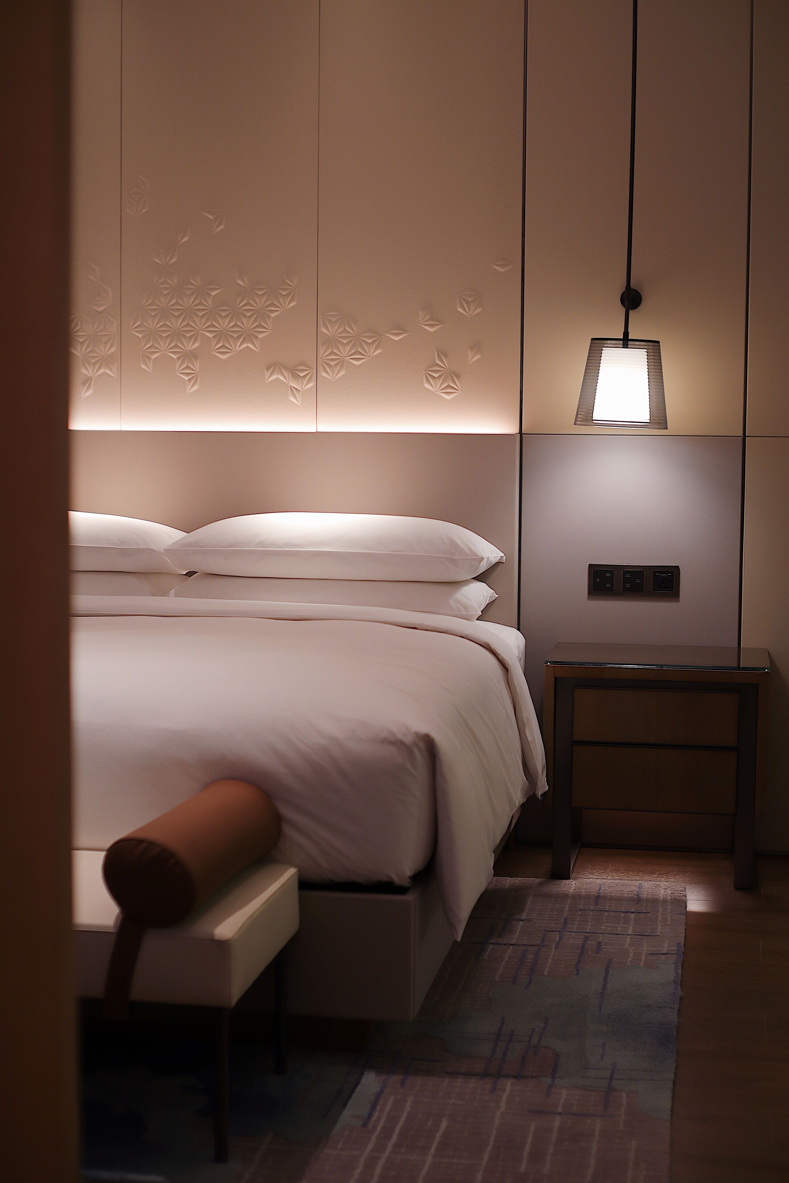 Un dormitorio ordenado con cama, mesita de noche y un banco.