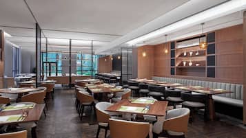 A modern restaurant interior with multiple dining tables and booths, wooden paneling, and pendant lighting.