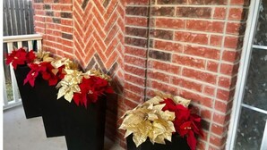 Eine Ziegelwand mit Zickzackmuster und zwei schwarze Pflanzgefäße mit roten und goldenen Weihnachtssternen.
