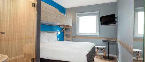 A modern hotel room with a bunk bed, a small desk, a TV, and a shower area.