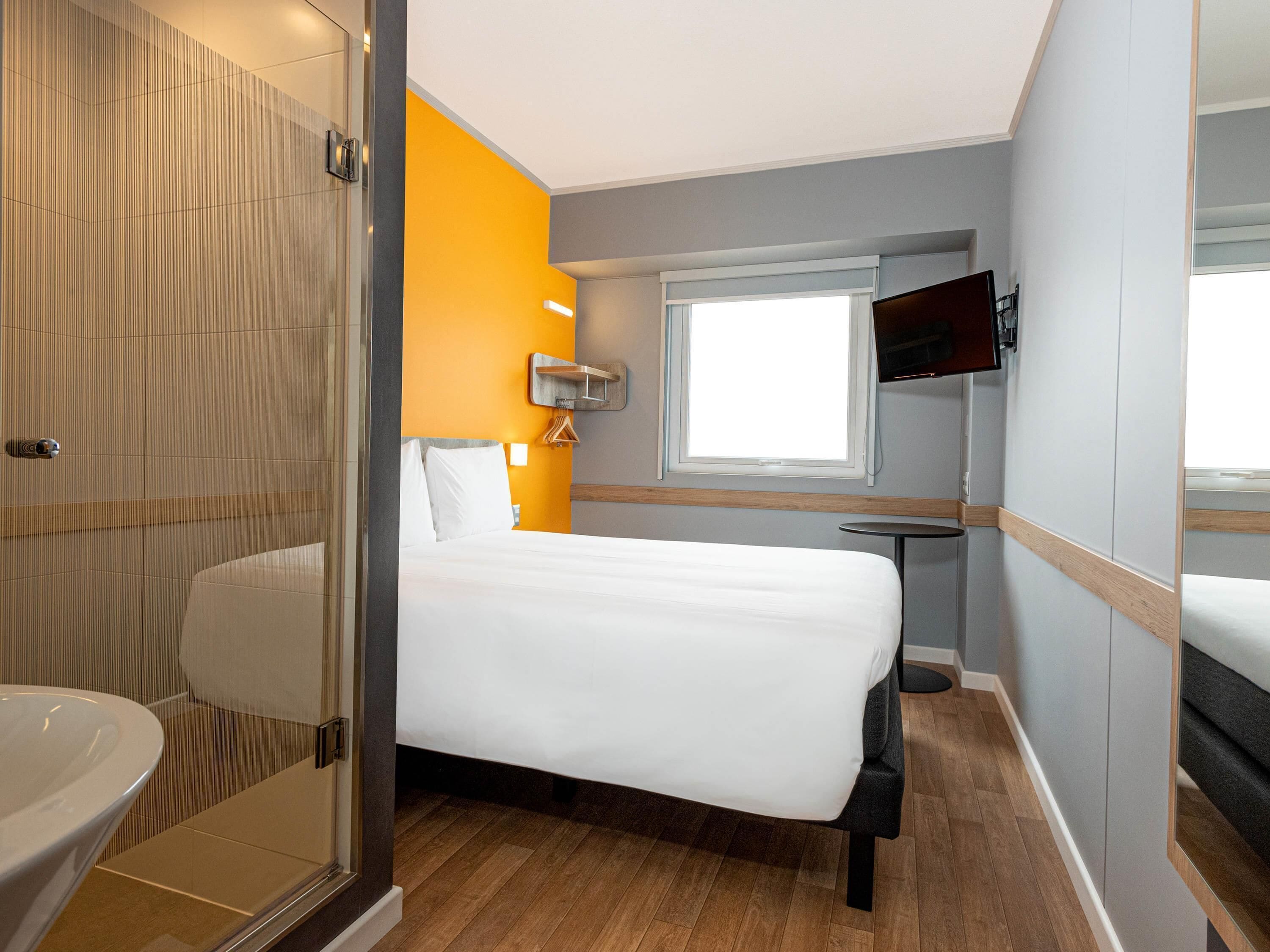 A hotel room with a bed, a bathroom, a window, and a TV.