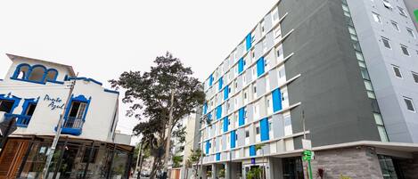 A modern hotel with a blue and white facade, multiple floors, and a visible entrance.