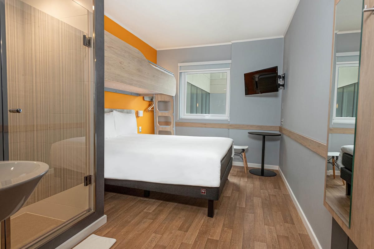 Quarto de hotel moderno com cama, mesa de cabeceira e um espelho grande.