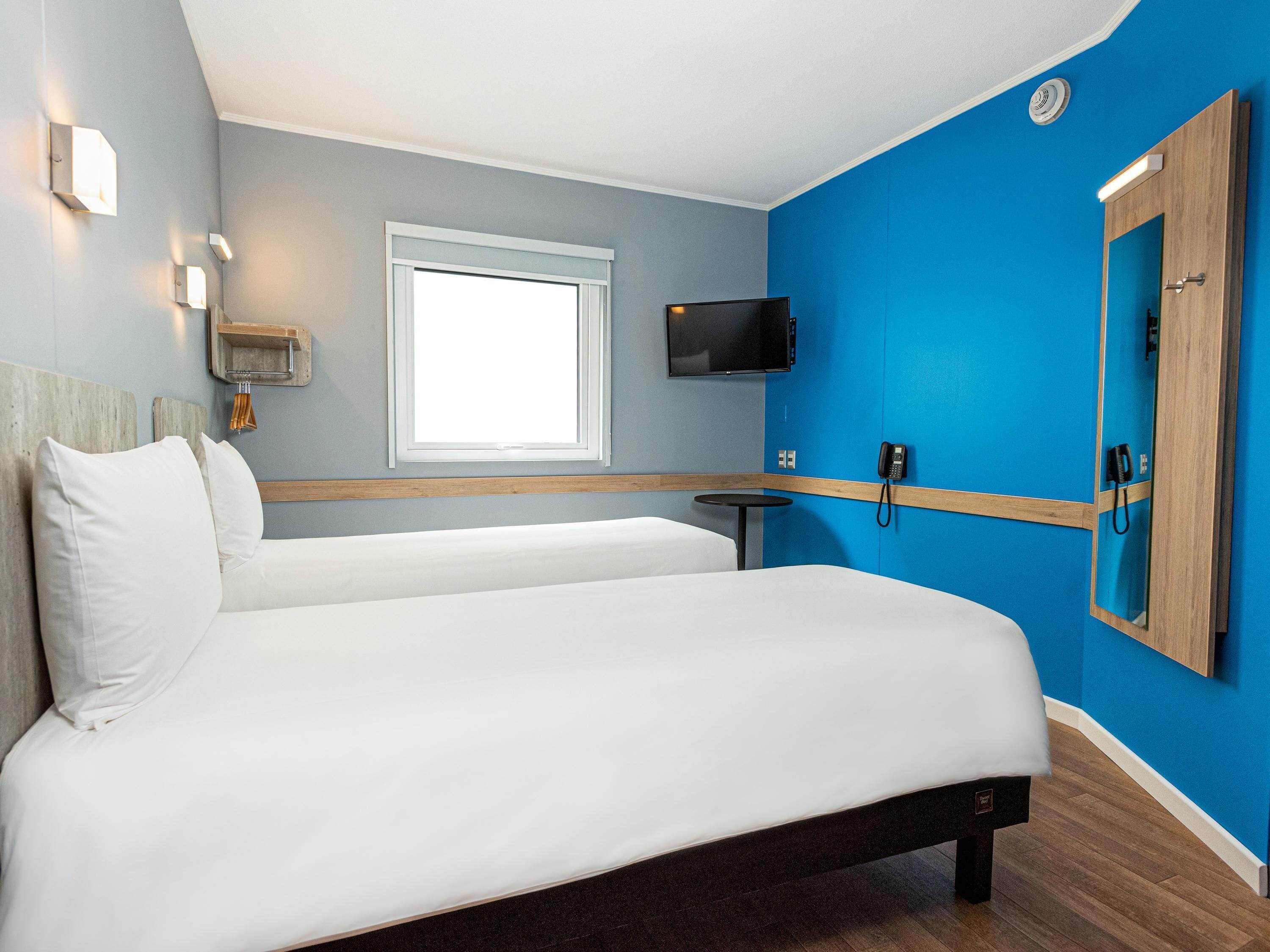 A hotel room with a bed, a television, a window, and a phone on the wall.