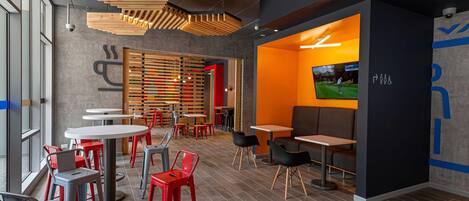 Interior moderno de restaurante com várias áreas de estar, incluindo mesas e cadeiras, e uma televisão exibindo uma partida de golfe.