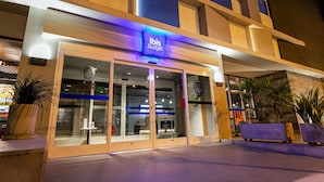 A modern building with a glass facade, a sign reading "ibis Budget," and outdoor seating with potted plants. - ibis Budget Lima Miraflores (Lima)