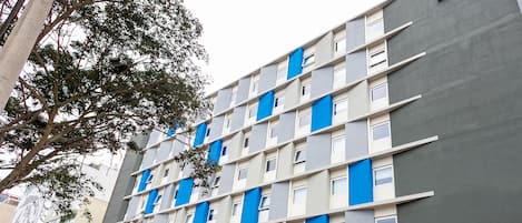A modern hotel with a grey and blue facade, multiple balconies, and a visible entrance with a sign.