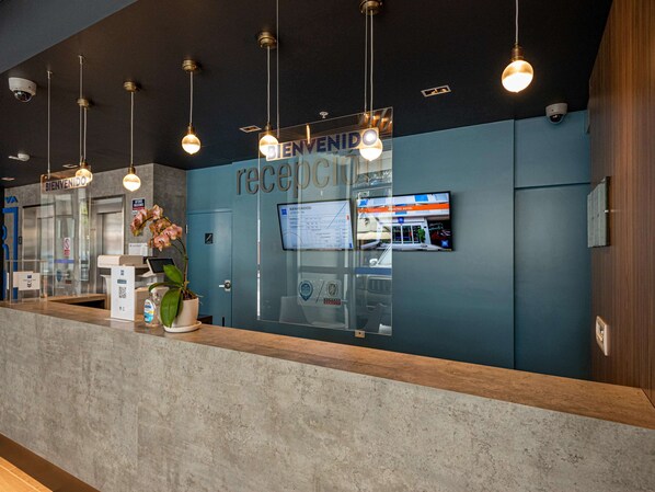 A reception area with a blue wall, a reception desk, and a monitor displaying hotel information.