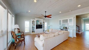 A spacious living room with a large sofa, a television, and a ceiling fan. - EnJoy the View: 4  BR, 3  BA House in Crystal Beach, Sleeps 13 (Bolivar Peninsula)