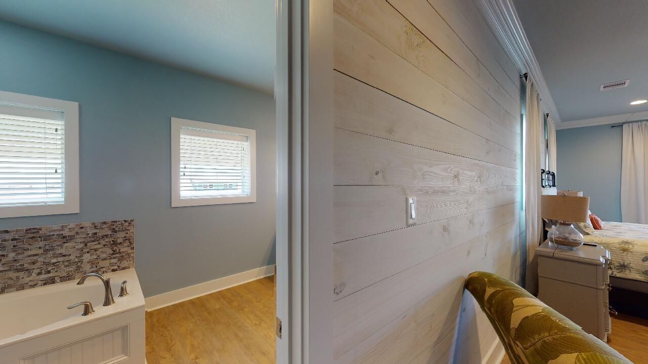 A room with a wooden wall, a bed, a nightstand, a lamp, and a window with blinds.