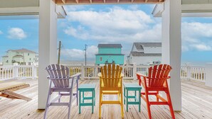 A wooden deck with four Adirondack chairs facing a beach with houses in the background. - EnJoy the View: 4  BR, 3  BA House in Crystal Beach, Sleeps 13 (Bolivar Peninsula)