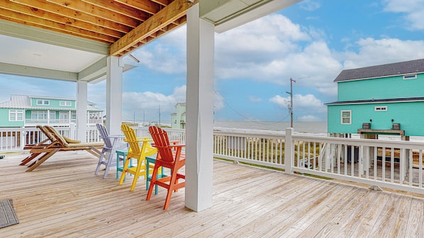 A wooden deck with colorful Adirondack chairs, a white railing, and a view of the ocean.