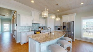 A spacious kitchen with white cabinetry, a granite island, stainless steel appliances, and pendant lighting. - EnJoy the View: 4  BR, 3  BA House in Crystal Beach, Sleeps 13 (Bolivar Peninsula)