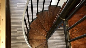 Un escalier en colimaçon avec des marches en bois et une rampe en métal, menant à un niveau inférieur.