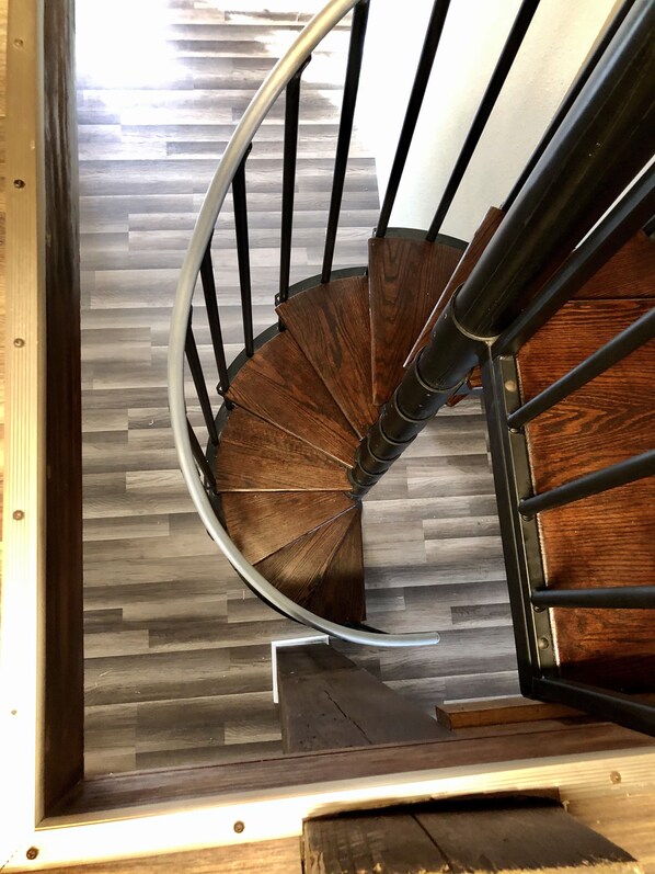 A spiral staircase with a wooden finish and metal railings, leading to a lower level.