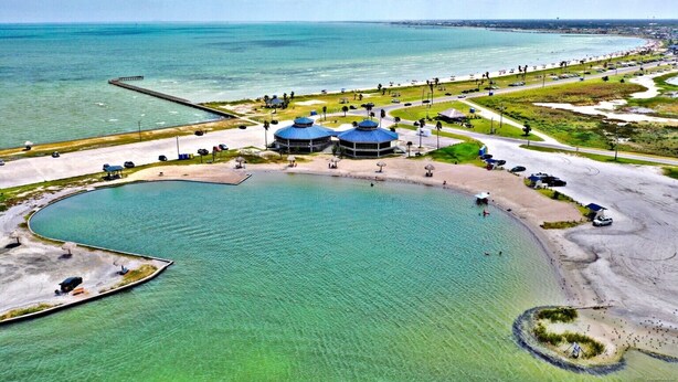 Vue aérienne d’une zone côtière avec une grande installation circulaire remplie d’eau, un bâtiment central doté d’un toit bleu et une jetée qui s’avance dans l’eau.
