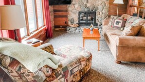 A cozy living room with a stone fireplace, a television mounted on the wall, a sofa, a coffee table, and a lamp.