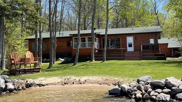 A cabin with a clear stream in front, surrounded by trees.