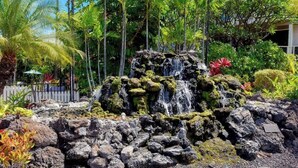 Catarata rodeada de vegetación tropical y una cerca blanca de piquetes.