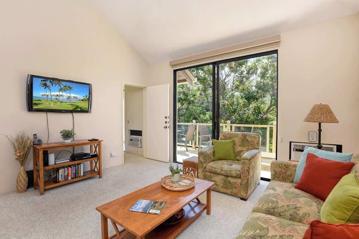 Un salon comprenant une télévision, une bibliothèque, une table basse, un canapé et un balcon avec vue sur les arbres.