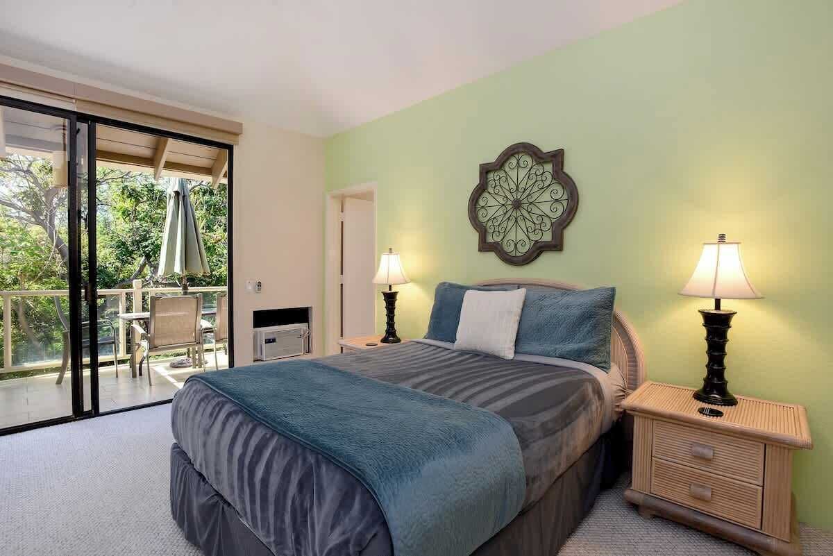 Une chambre avec un lit, deux lampes de chevet, un élément décoratif mural, une porte-fenêtre coulissante donnant sur un balcon et une petite table avec des chaises.