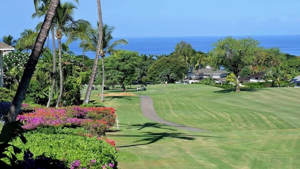 Un campo de golf con vista despejada al océano, rodeado de exuberante vegetación y palmeras.