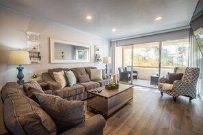 A spacious living room with a large sofa set, a coffee table, and a view through a sliding glass door to an outdoor patio.