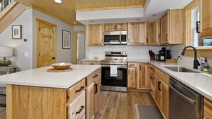 A modern kitchen with wooden cabinets, stainless steel appliances, and a central island. - New Log Cabin in the Valley, Elk Experience, Year Round Access (Maggie Valley)