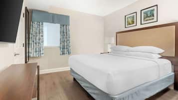 Ein Hotelzimmer mit einem Bett, einem Schreibtisch, einem Fenster mit Vorhängen und zwei gerahmten Bildern an der Wand.