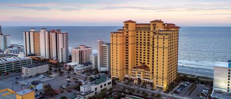 A high-rise hotel with multiple floors, a parking lot, and a view of the ocean.