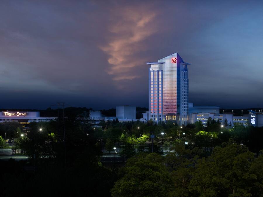 A high-rise hotel with a prominent logo on the top, surrounded by trees and other buildings.