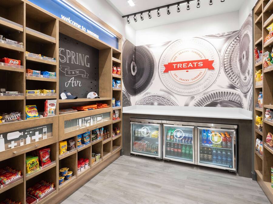 A snack and beverage display area with shelves stocked with various snacks and drinks, and a wall with a 'Spring is the Air' sign and a 'Treats' sign.