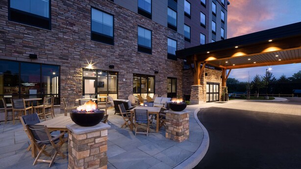 An outdoor patio with stone walls, wooden furniture, and a fire feature. - Hampton Inn Verona at Turning Stone (Verona)