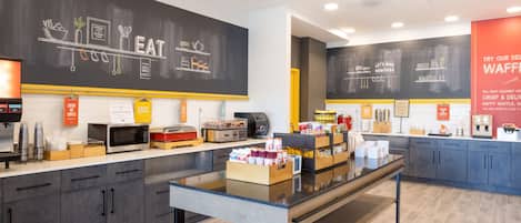 Um café moderno com cardápio em lousa, estação de café por autoatendimento e um balcão com diversas opções de comida.