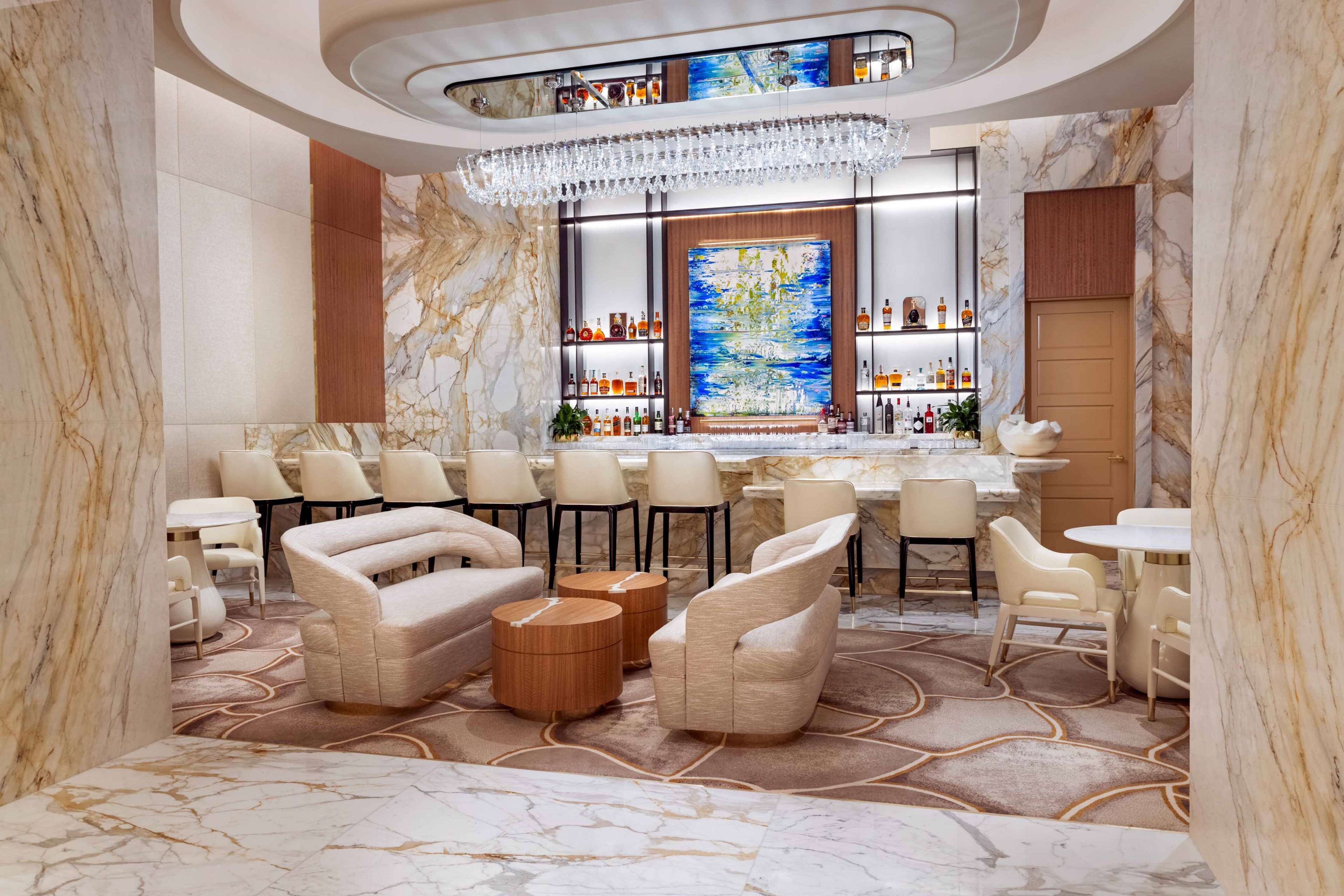 A luxurious bar area with marble flooring, plush seating, and a large, colorful artwork on the wall.