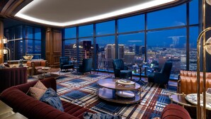 Une chambre d’hôtel située dans un immeuble de grande hauteur, offrant une vue imprenable sur la ville, dotée de fauteuils confortables et d’un sol à motifs.