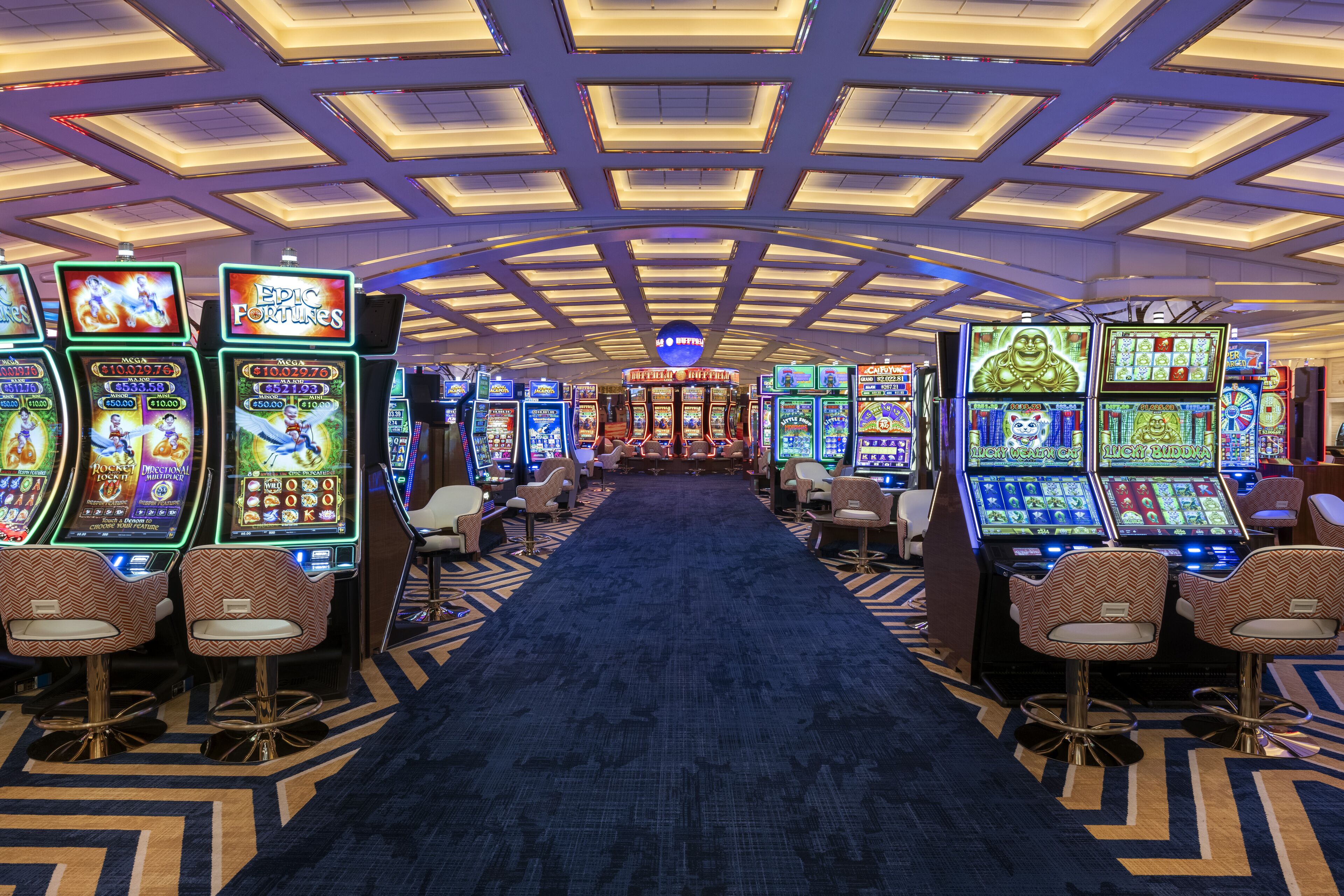A casino with multiple slot machines and bar seating along a central carpeted walkway.