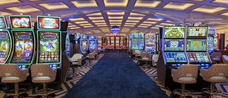 A casino with multiple slot machines and bar seating along a central carpeted walkway.