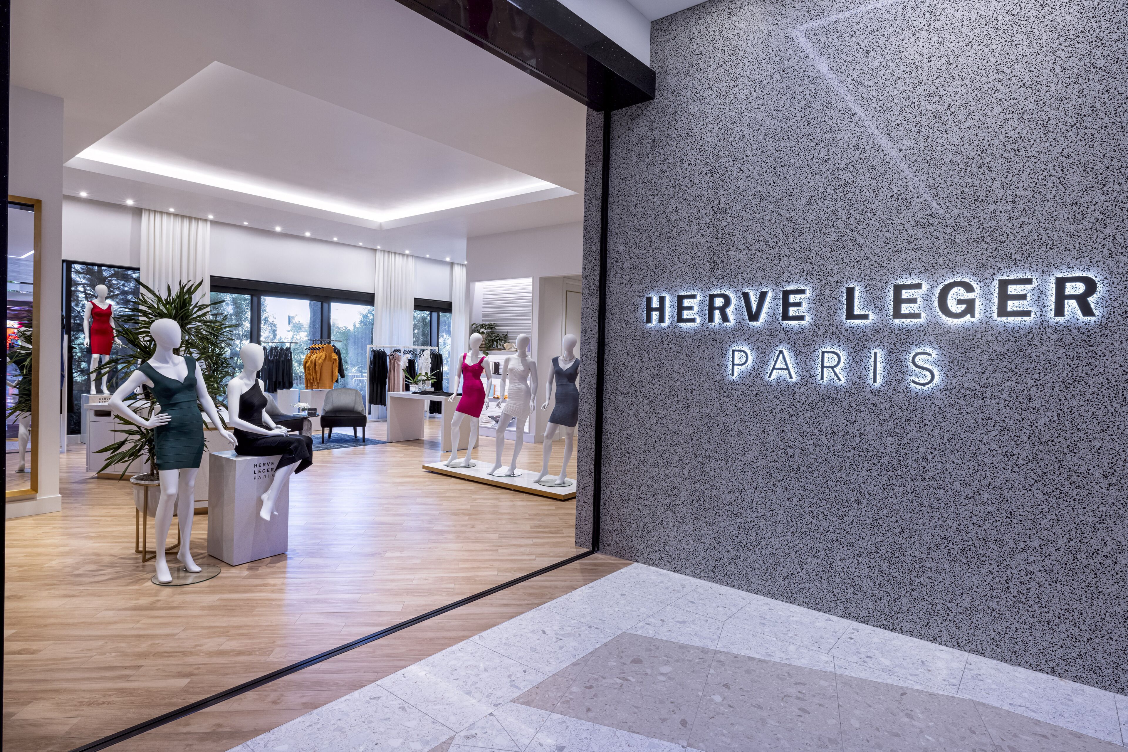 A modern interior of Herve Leger Paris with mannequins displaying clothing, a clean design, and large windows.