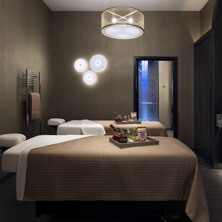 A modern hotel room with a large bed, a sitting area, a vanity with a mirror, and a small window.