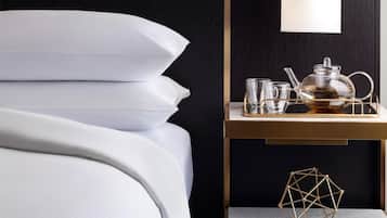 A neatly made bed with white linens, a bedside table with a tea set, and a geometric sculpture.